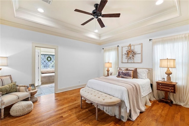 bedroom with ensuite bathroom, light wood-type flooring, ornamental molding, a tray ceiling, and ceiling fan