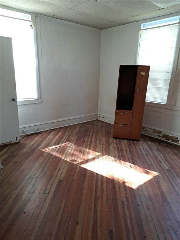 unfurnished bedroom with hardwood / wood-style floors, a drop ceiling, and baseboards