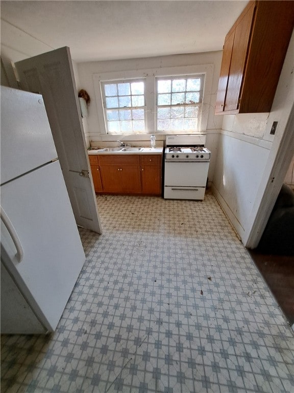 kitchen with white appliances, a sink, light countertops, light floors, and brown cabinetry