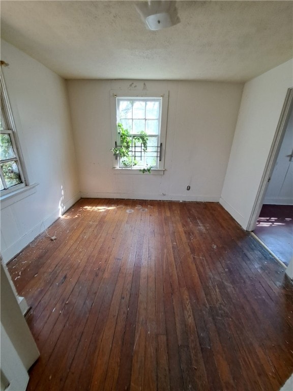 empty room with a textured ceiling, wood-type flooring, and baseboards