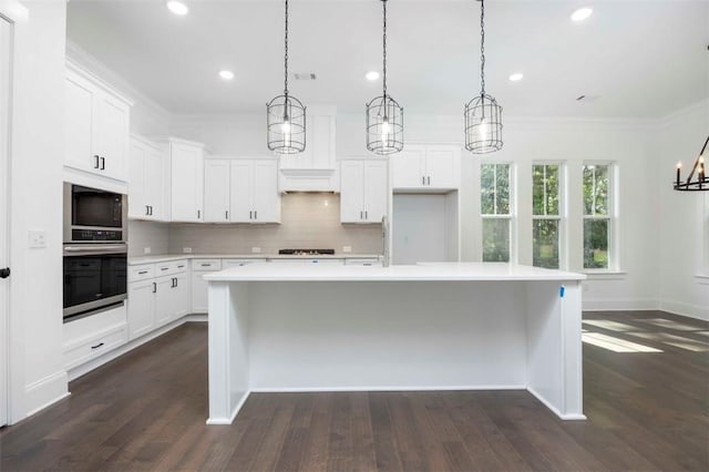 kitchen featuring decorative light fixtures, white cabinetry, a kitchen island with sink, and oven