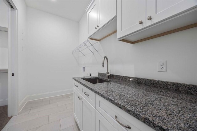 kitchen with sink, white cabinets, dark stone counters, and light tile patterned floors