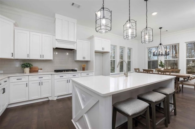 kitchen featuring white cabinets, decorative light fixtures, an island with sink, decorative backsplash, and sink