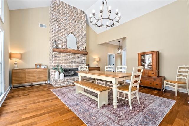 dining space featuring high vaulted ceiling, a notable chandelier, a fireplace, wood finished floors, and visible vents