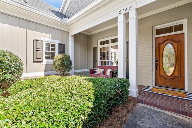 entrance to property featuring board and batten siding, roof with shingles, a porch, and brick siding