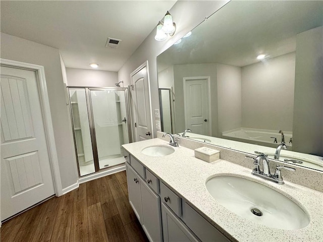 bathroom with a stall shower, a sink, wood finished floors, and visible vents