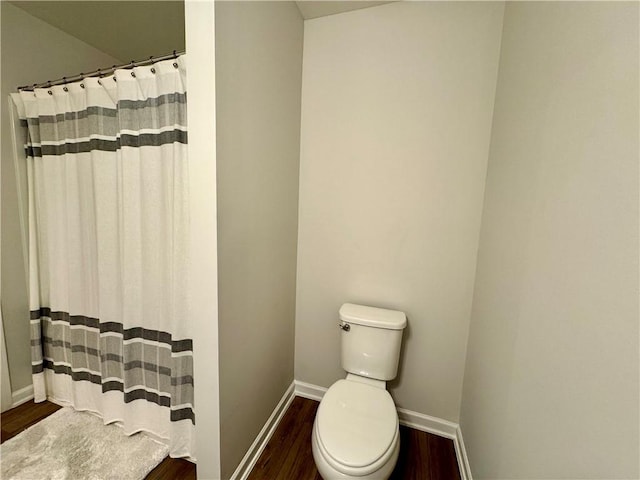 bathroom with wood finished floors, toilet, a shower with shower curtain, and baseboards