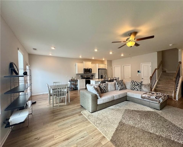 living area with baseboards, stairway, ceiling fan, and light wood-style floors
