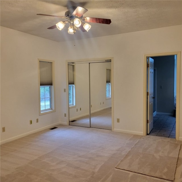 unfurnished bedroom with ceiling fan, light colored carpet, a textured ceiling, and a closet