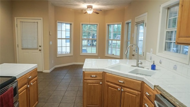 kitchen with dishwasher, dark tile patterned flooring, sink, ceiling fan, and tile counters