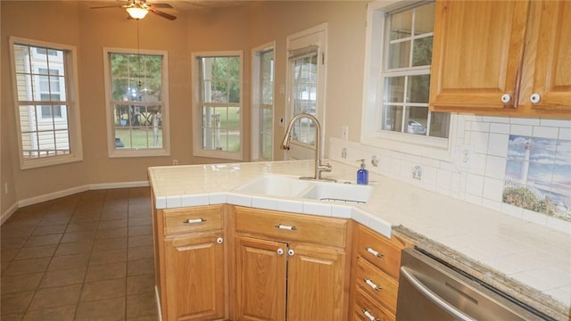 kitchen featuring stainless steel dishwasher, ceiling fan, dark tile patterned floors, sink, and tile counters