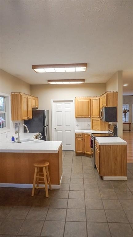 kitchen featuring a breakfast bar, tile patterned floors, sink, appliances with stainless steel finishes, and kitchen peninsula