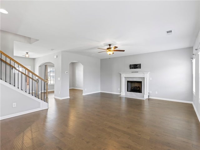 unfurnished living room featuring dark wood-style floors, visible vents, a ceiling fan, a fireplace with flush hearth, and stairs