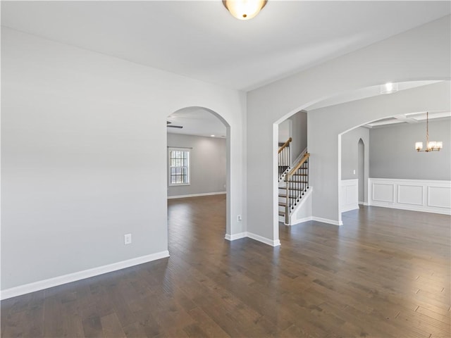 spare room featuring stairs, wood finished floors, arched walkways, and baseboards