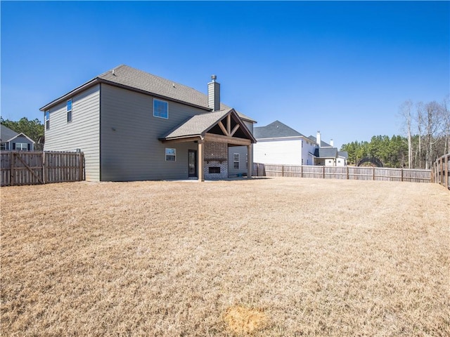 back of house with a lawn, a chimney, and a fenced backyard