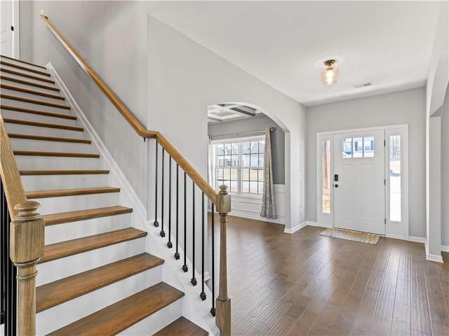 foyer entrance with visible vents, dark wood-type flooring, baseboards, stairs, and arched walkways