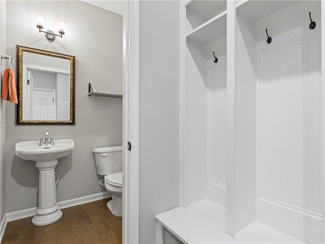 bathroom with toilet, wood finished floors, baseboards, and a shower