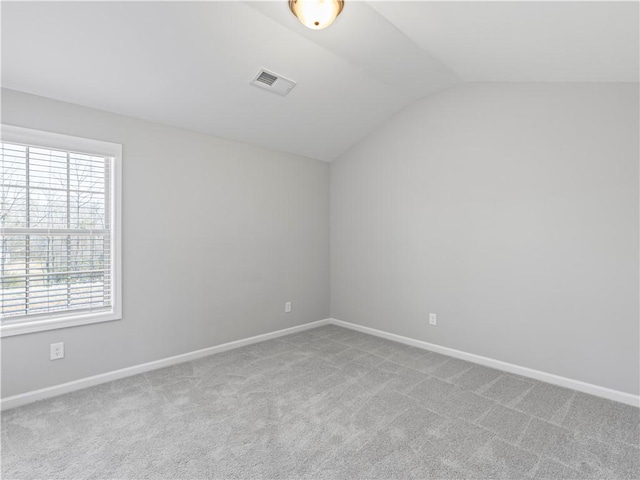 carpeted spare room featuring vaulted ceiling, baseboards, and visible vents