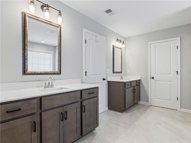 full bath with two vanities, baseboards, visible vents, and a sink