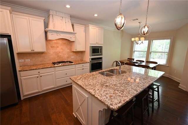 kitchen with a kitchen island with sink, backsplash, appliances with stainless steel finishes, a sink, and custom exhaust hood