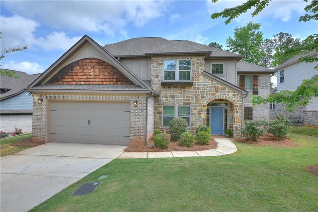 view of front of property with a front lawn, stone siding, roof with shingles, an attached garage, and driveway