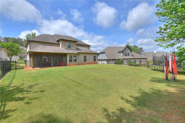 back of house featuring a lawn, a sunroom, a fenced backyard, and a trampoline