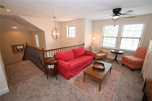 carpeted living room with baseboards and ceiling fan with notable chandelier
