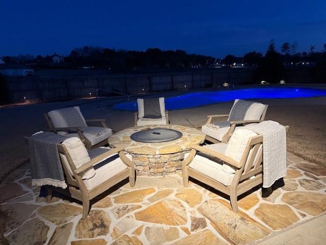 patio at twilight with a fire pit and a fenced in pool