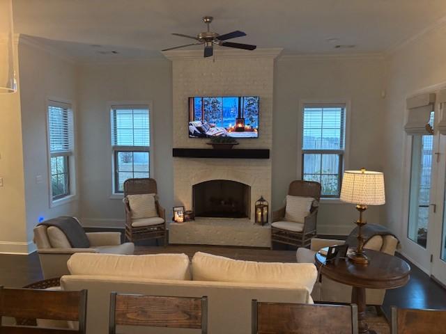 living room with ceiling fan, a wealth of natural light, crown molding, and a fireplace