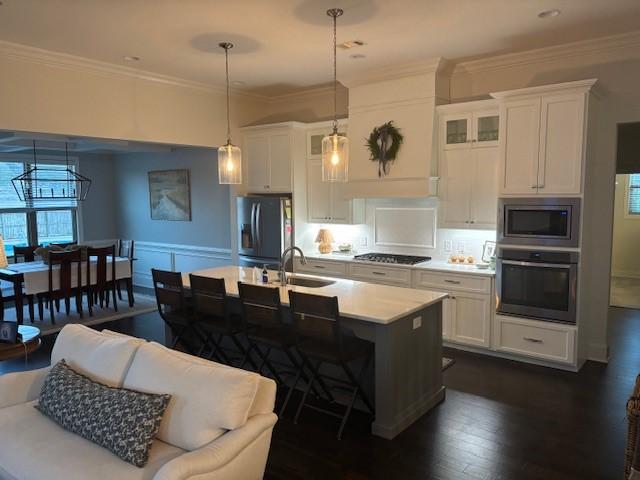 kitchen featuring appliances with stainless steel finishes, hanging light fixtures, white cabinets, and a kitchen island with sink