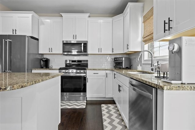 kitchen featuring appliances with stainless steel finishes, white cabinetry, sink, backsplash, and light stone countertops