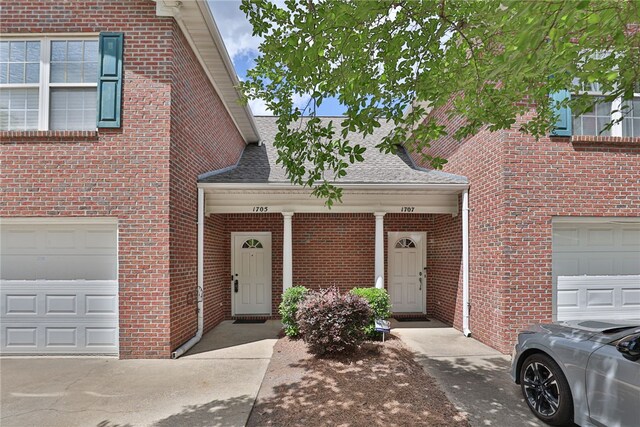 property entrance featuring a shingled roof, brick siding, and an attached garage