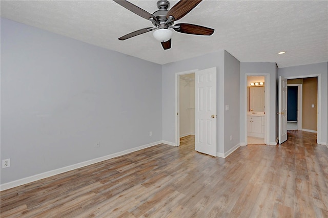 unfurnished bedroom with baseboards, light wood-type flooring, a walk in closet, ensuite bath, and recessed lighting