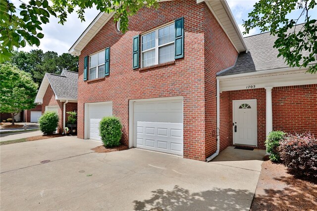 traditional home with driveway, brick siding, an attached garage, and roof with shingles