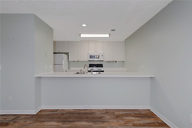 kitchen with white appliances, a peninsula, a sink, recessed lighting, and wood finished floors