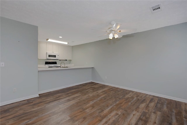 kitchen with white microwave, stove, a sink, baseboards, and recessed lighting