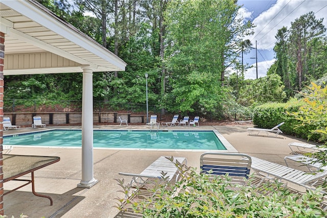 community pool with a patio area, fence, and view of wooded area