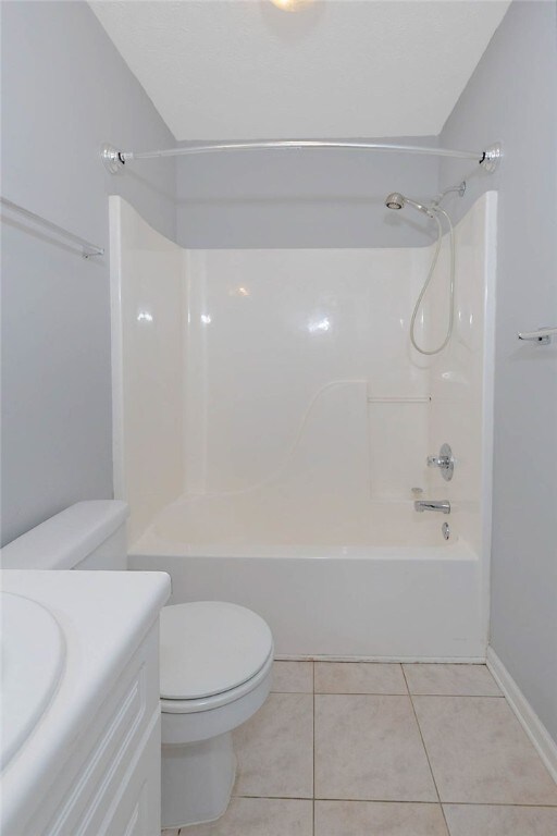 bathroom featuring toilet, tile patterned flooring, vanity, shower / tub combination, and baseboards