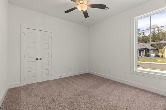 carpeted spare room featuring a ceiling fan and baseboards