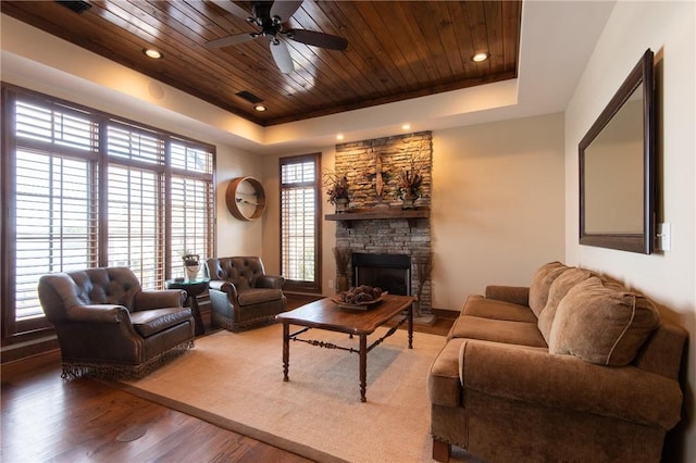 living room featuring a stone fireplace, a tray ceiling, wooden ceiling, and wood finished floors