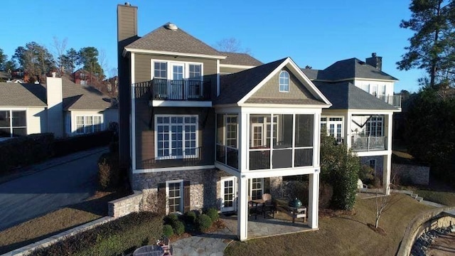 back of property with a patio, a balcony, stone siding, a sunroom, and a chimney