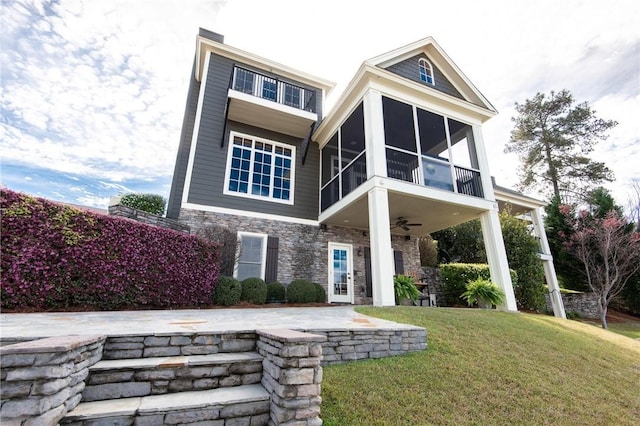 back of property with stone siding, a lawn, a sunroom, and a ceiling fan