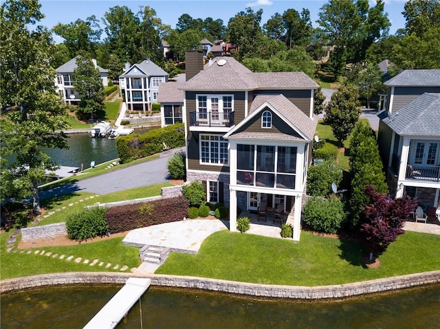 back of property featuring a balcony, stone siding, a chimney, a water view, and a patio area