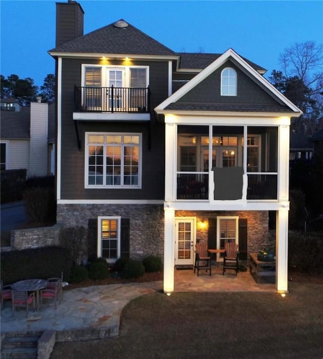 rear view of house featuring a patio, a chimney, a sunroom, a balcony, and stone siding