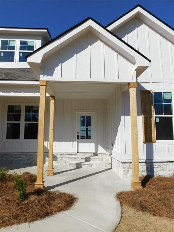 view of exterior entry with roof with shingles, a porch, and board and batten siding