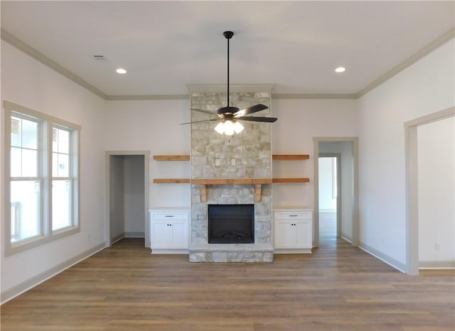 unfurnished living room with crown molding, a stone fireplace, baseboards, and wood finished floors