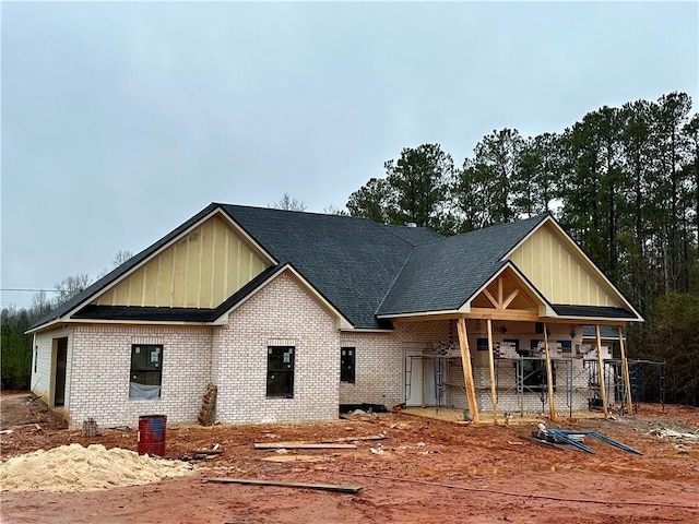 view of front of home featuring brick siding, board and batten siding, and a shingled roof