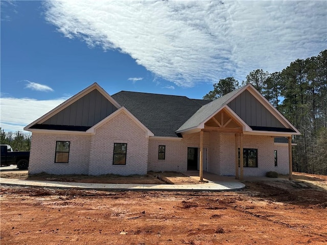 view of front facade with board and batten siding, brick siding, and a patio