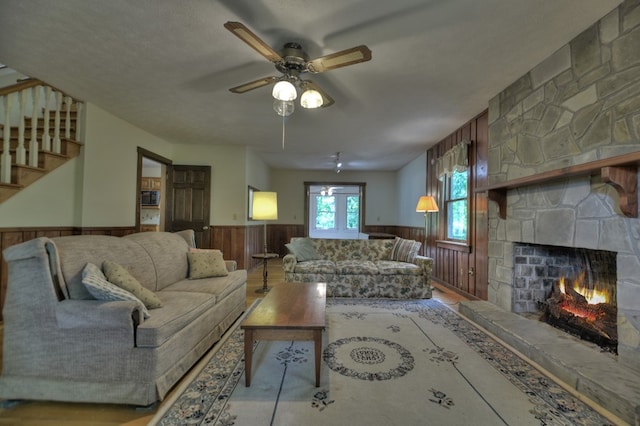 living room with light hardwood / wood-style floors, a stone fireplace, wood walls, a textured ceiling, and ceiling fan