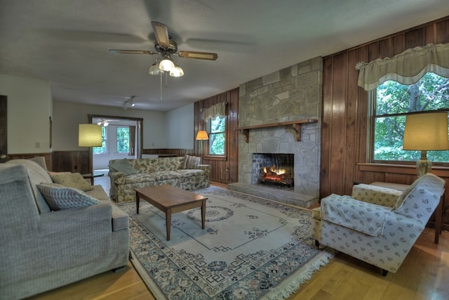 living room featuring a fireplace, a textured ceiling, ceiling fan, wooden walls, and hardwood / wood-style floors